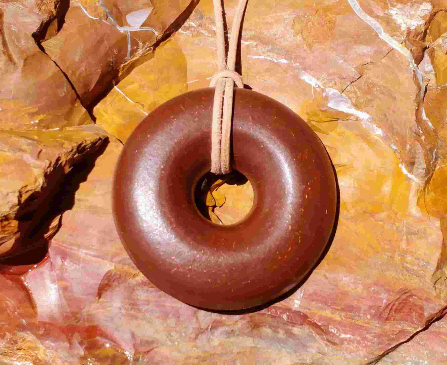 A brown donut-shaped Orgonite pendant with a leather necklace cord, placed against a background of red rocks. andy orgone emf sedona vortex jewlery red