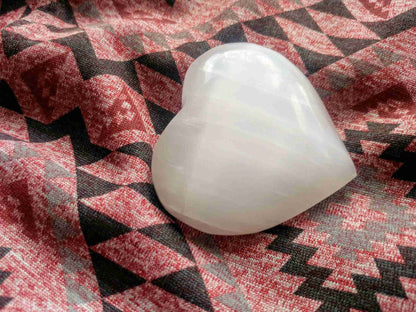 White Selenite Puffy Heart – Reiki Healing Crystal & Energy Cleanser displayed on patterned fabric. Ideal for meditation and energy work.