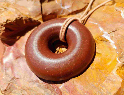 A brown donut-shaped Orgonite pendant with a leather necklace cord, placed against a background of red rocks. andy orgone emf sedona vortex jewlery red