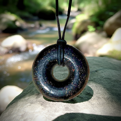 Orgonite Pendant on a rock near a stream, showcasing a black sun orgone energy generator crystal necklace.