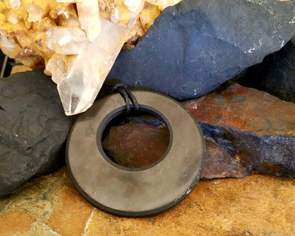 Black Shungite Eclipse Pendant with round 2-inch design for EMF protection and energy healing, displayed on natural stone background.