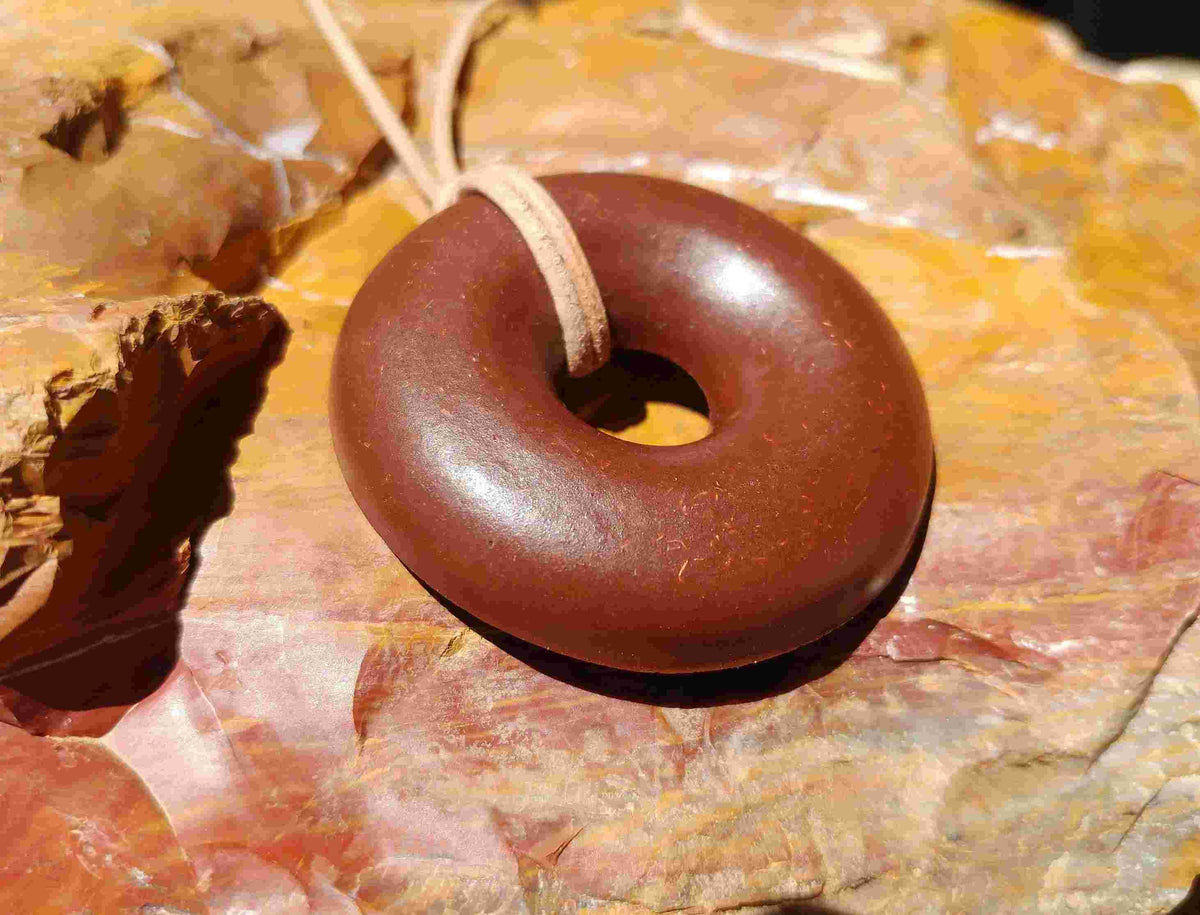A brown donut-shaped Orgonite pendant with a leather necklace cord, placed against a background of red rocks. andy orgone emf sedona vortex jewlery red